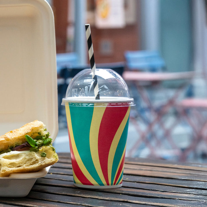 Packaging Wise 12oz patterned cold drink cup with dome lid — colourful takeaway cup ideal for iced coffee, milkshakes & juices, shown outdoors on café table.